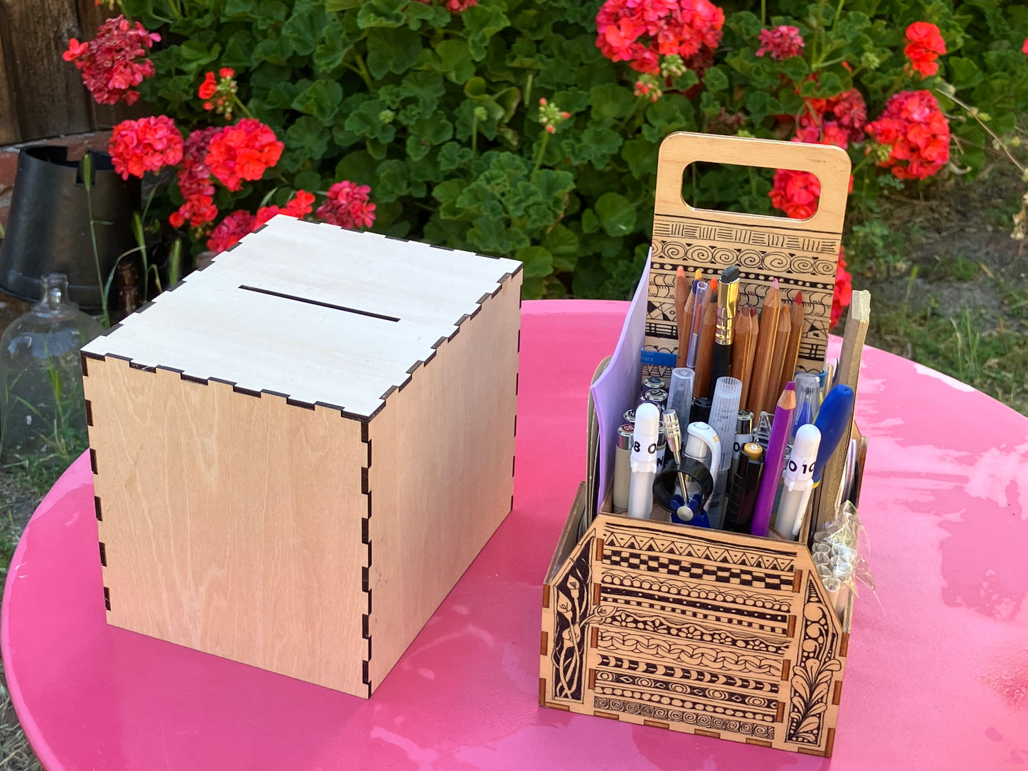 Wooden card box and pen holder on a pink surface with flowers in the background